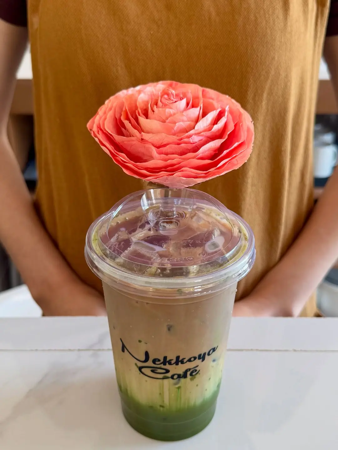 An iced latte in a Nekkoya cup topped with a fresh rose
