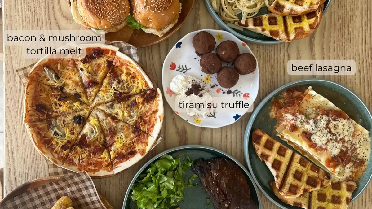 A table full of café food: sliders, sardine pesto pasta, tortilla melts, lasagna, ribs and desserts