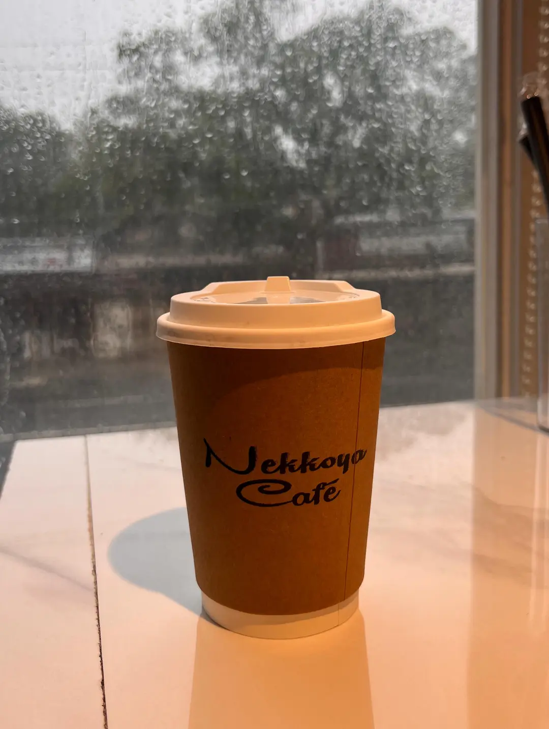 A Nekkoya Café hot cup against a rain-streaked window