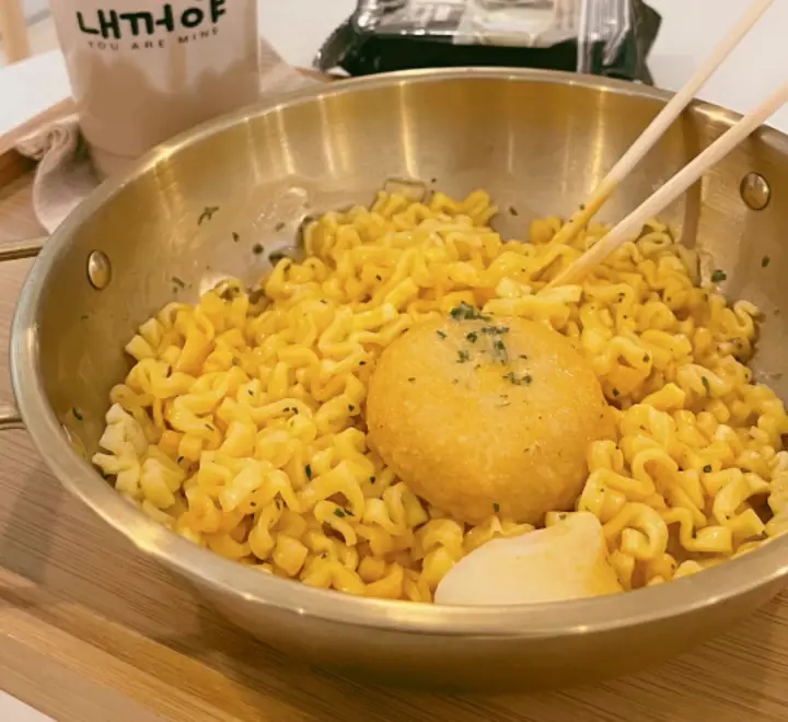 A gold DIY pot of cheesy ramyeon topped with a fried patty